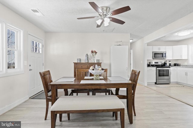 dining room with light wood-type flooring, visible vents, a textured ceiling, and baseboards