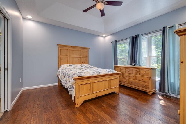 bedroom with a raised ceiling, ceiling fan, and dark hardwood / wood-style flooring