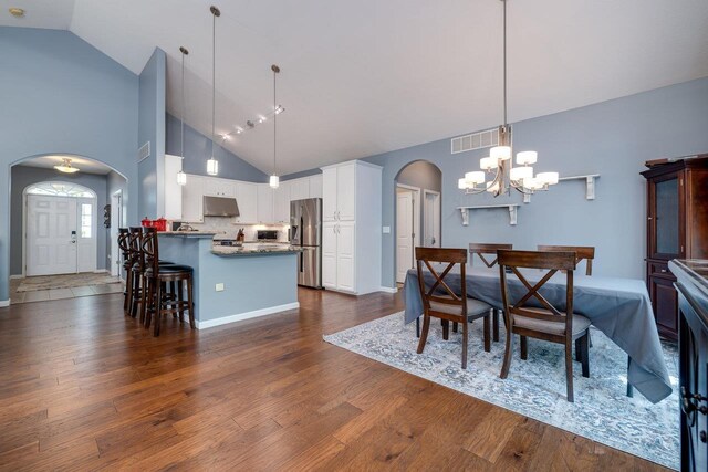 dining space featuring dark hardwood / wood-style flooring, high vaulted ceiling, and an inviting chandelier