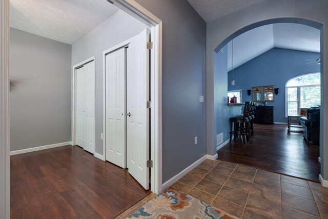 hall with vaulted ceiling, dark hardwood / wood-style floors, and a textured ceiling