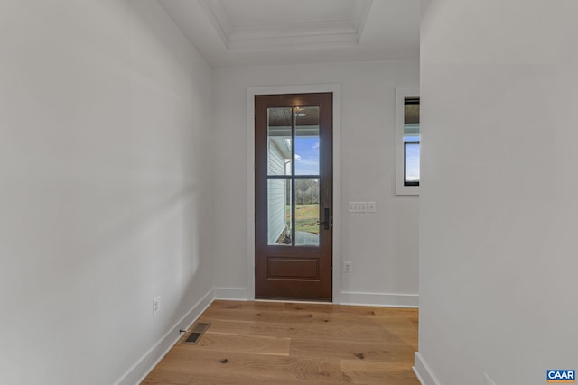 doorway to outside with visible vents, light wood-style flooring, baseboards, crown molding, and a raised ceiling