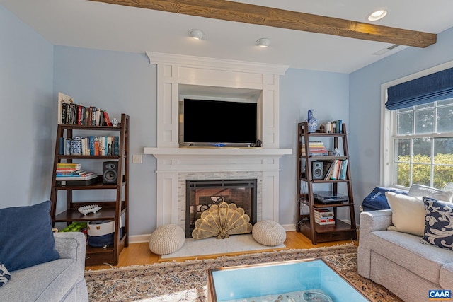 living area with beamed ceiling, a fireplace, baseboards, and wood finished floors