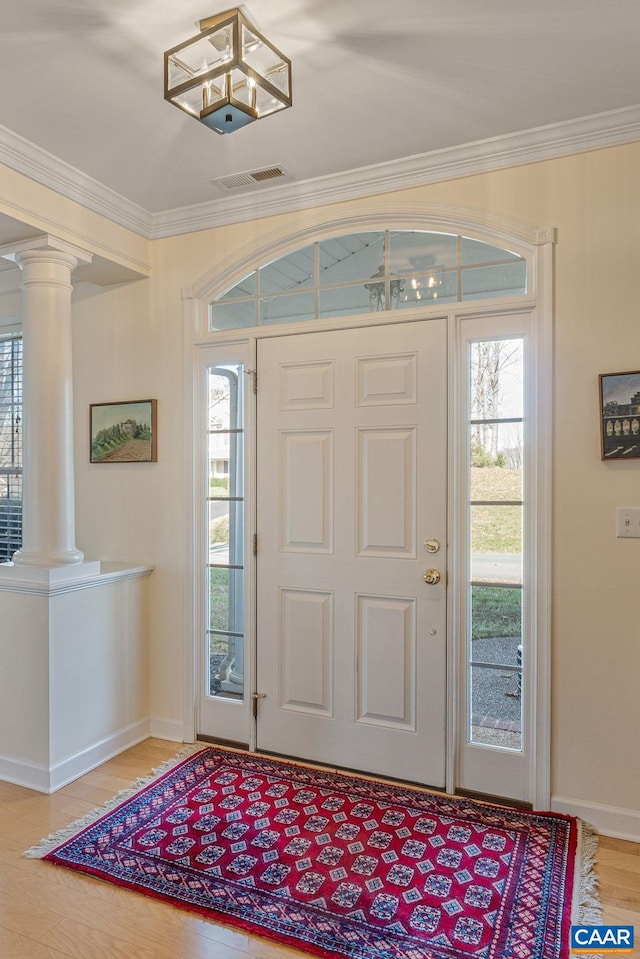 foyer entrance with light wood-style flooring, baseboards, crown molding, and ornate columns