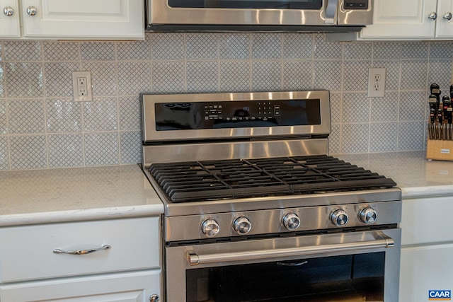 kitchen with light stone counters, backsplash, white cabinets, and stainless steel range with gas cooktop