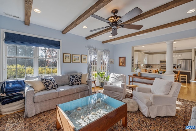 living area featuring visible vents, decorative columns, beam ceiling, wood finished floors, and a ceiling fan