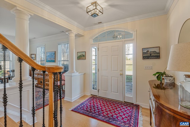 foyer entrance with crown molding, a wealth of natural light, light wood finished floors, and ornate columns