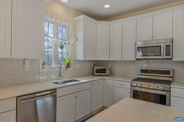 kitchen with a sink, backsplash, appliances with stainless steel finishes, and white cabinets