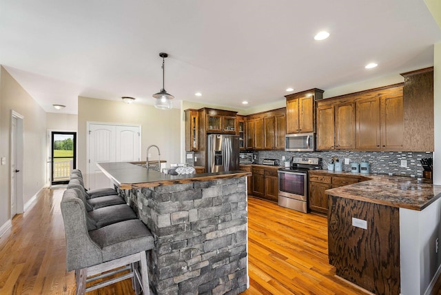 kitchen with dark countertops, glass insert cabinets, light wood-style floors, tasteful backsplash, and stainless steel appliances