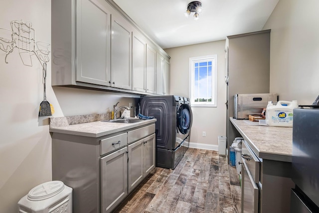 clothes washing area featuring washing machine and dryer, baseboards, dark wood-type flooring, a sink, and cabinet space