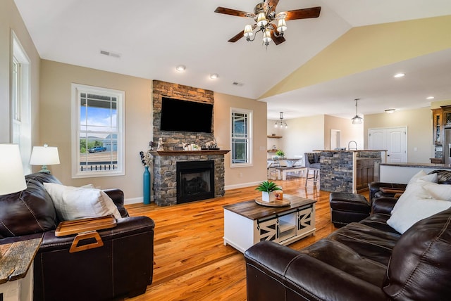 living room with light wood finished floors, a fireplace, a ceiling fan, lofted ceiling, and visible vents