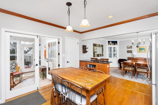 dining space featuring a notable chandelier, crown molding, light hardwood / wood-style flooring, and french doors