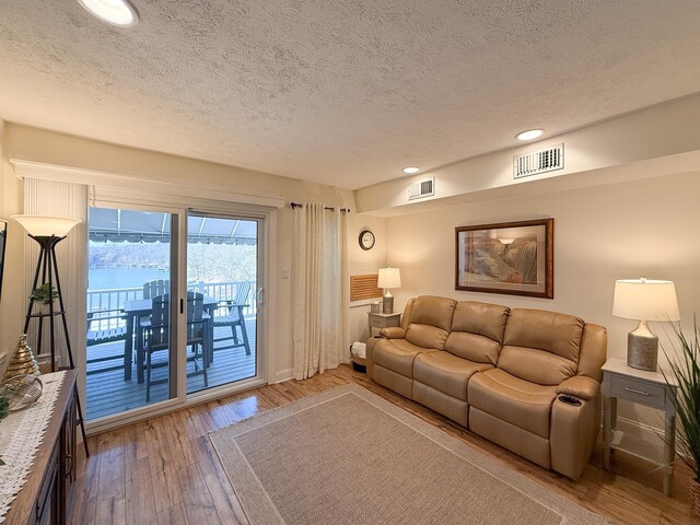 living room with a water view, light hardwood / wood-style flooring, and a textured ceiling