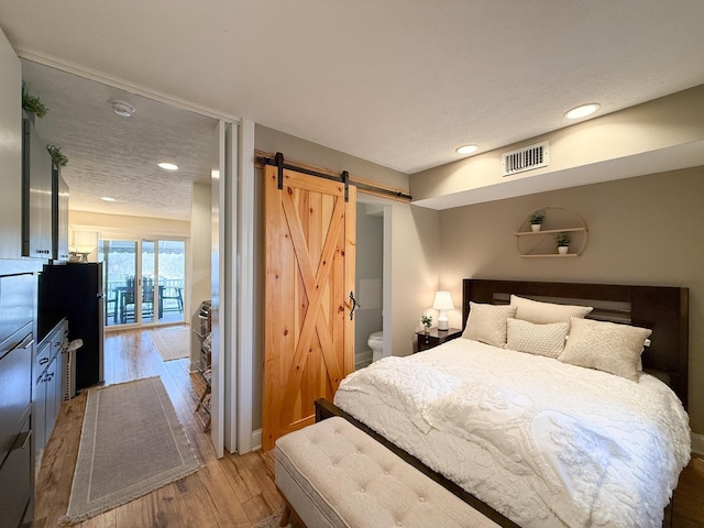 bedroom with wood-type flooring, a barn door, a textured ceiling, and ensuite bathroom