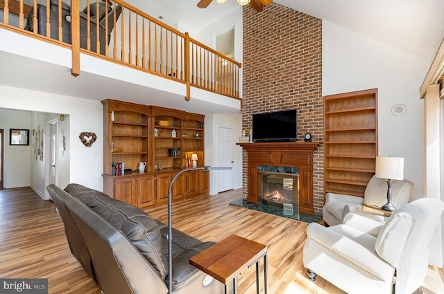 living area featuring light wood-type flooring, beam ceiling, a fireplace, high vaulted ceiling, and a ceiling fan