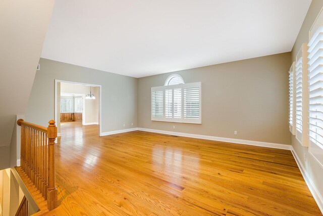 empty room featuring an inviting chandelier, a healthy amount of sunlight, and light wood-type flooring