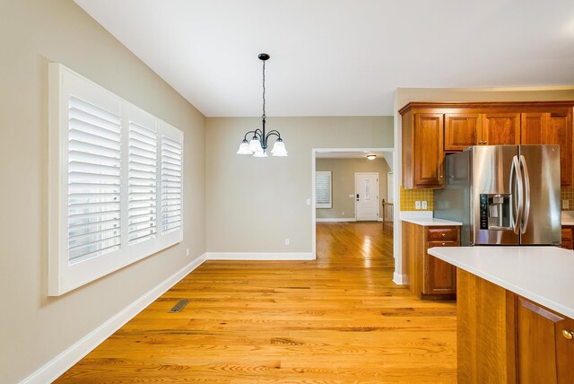 kitchen with light hardwood / wood-style flooring, hanging light fixtures, stainless steel fridge, and an inviting chandelier