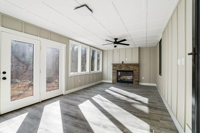 unfurnished living room featuring ceiling fan, a healthy amount of sunlight, a stone fireplace, and wood-type flooring