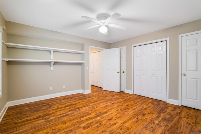 unfurnished bedroom with dark hardwood / wood-style flooring, two closets, and ceiling fan