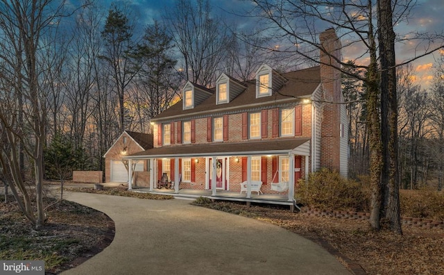 view of front of property with brick siding, a chimney, a porch, a garage, and driveway