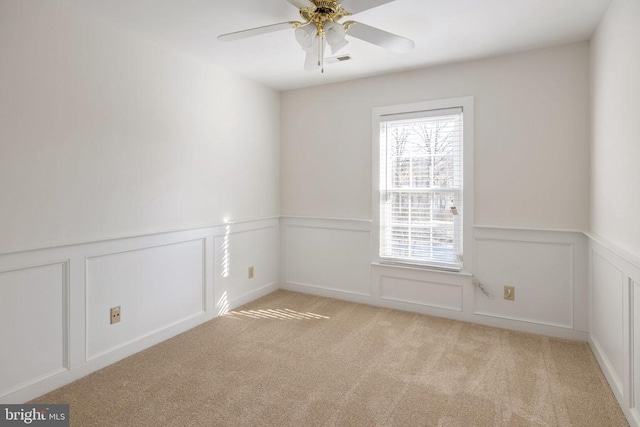 spare room with a decorative wall, light carpet, visible vents, a ceiling fan, and wainscoting