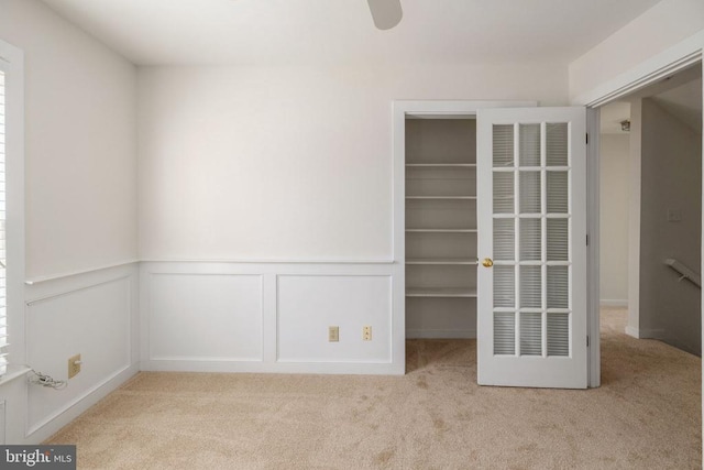 interior space featuring a decorative wall, a wainscoted wall, light colored carpet, a closet, and a walk in closet