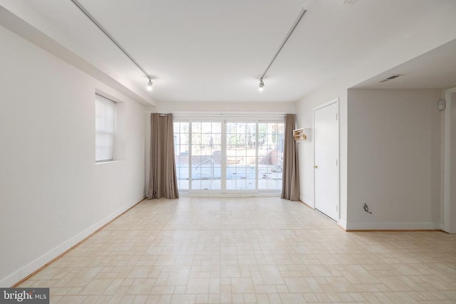 unfurnished room with baseboards, visible vents, and track lighting