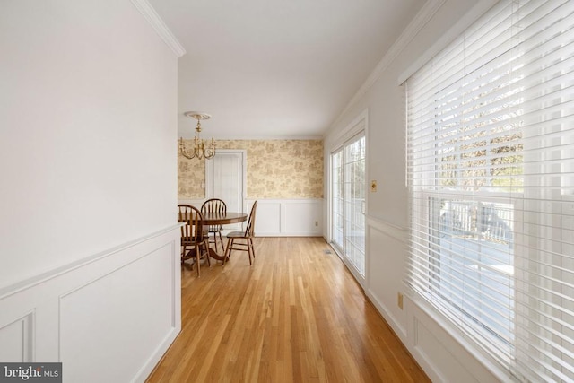 hallway featuring a wainscoted wall, a notable chandelier, ornamental molding, light wood-type flooring, and wallpapered walls