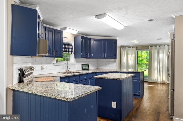 kitchen with a peninsula, blue cabinetry, visible vents, and a sink
