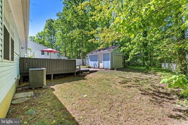 view of yard featuring an outbuilding, a wooden deck, a detached garage, central AC, and fence
