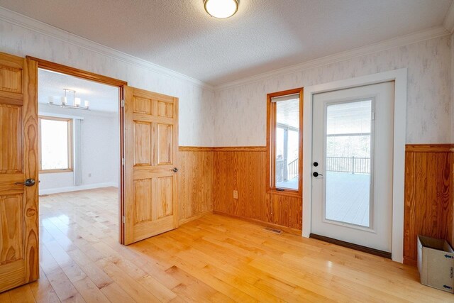 doorway featuring light hardwood / wood-style flooring, ornamental molding, and a textured ceiling