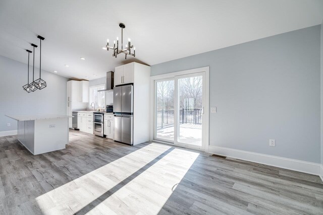 kitchen featuring a kitchen island, pendant lighting, white cabinets, stainless steel appliances, and wall chimney exhaust hood