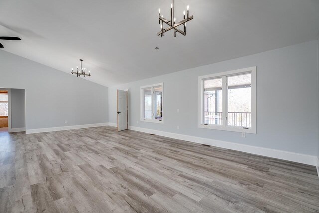 unfurnished living room featuring an inviting chandelier, lofted ceiling, plenty of natural light, and light wood-type flooring