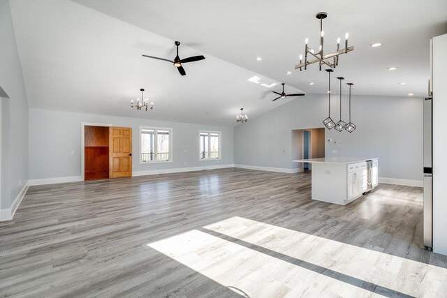 unfurnished living room with ceiling fan with notable chandelier, light hardwood / wood-style flooring, and high vaulted ceiling