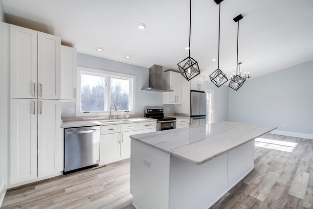 kitchen with wall chimney exhaust hood, hanging light fixtures, a kitchen island, stainless steel appliances, and white cabinets