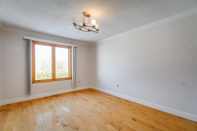 empty room featuring crown molding, light hardwood / wood-style flooring, a textured ceiling, and a chandelier