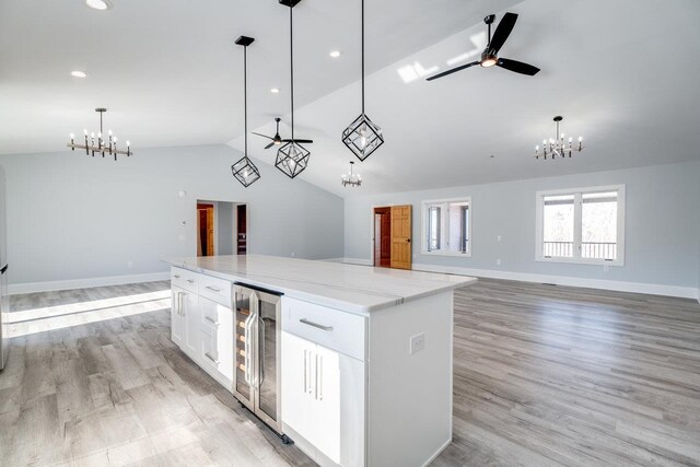 kitchen featuring white cabinetry, beverage cooler, hanging light fixtures, a center island, and light stone counters