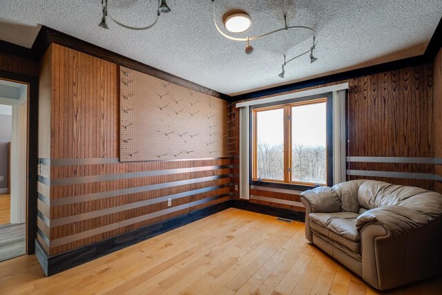 unfurnished room featuring track lighting, a textured ceiling, light hardwood / wood-style flooring, and wood walls