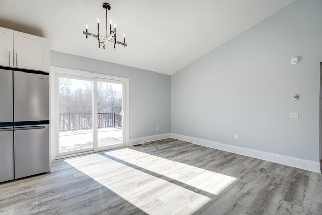 unfurnished dining area with vaulted ceiling, a chandelier, and light hardwood / wood-style floors