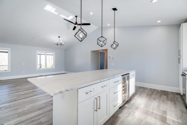 kitchen with white cabinetry, hanging light fixtures, light stone countertops, a kitchen island, and beverage cooler