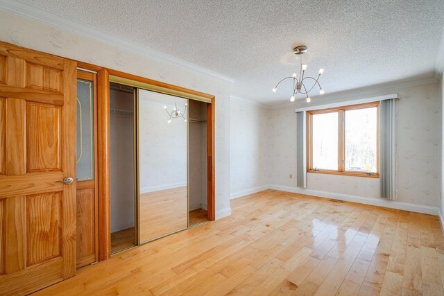 unfurnished bedroom featuring a notable chandelier, light hardwood / wood-style floors, crown molding, a textured ceiling, and a closet