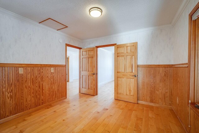 unfurnished room with ornamental molding, light hardwood / wood-style floors, wooden walls, and a textured ceiling