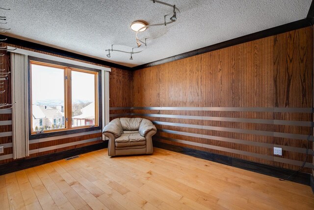 unfurnished room with rail lighting, wood-type flooring, wooden walls, and a textured ceiling