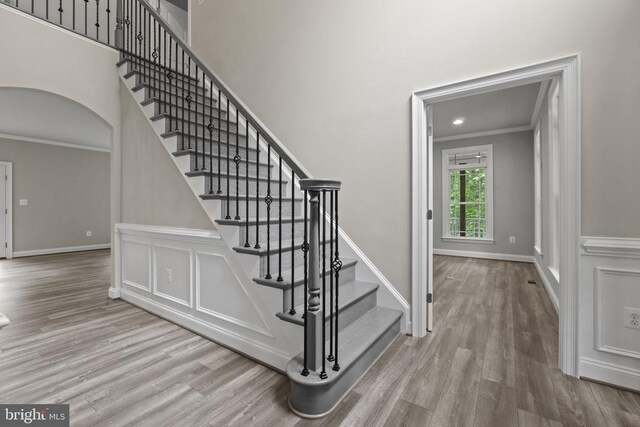 stairway with hardwood / wood-style floors, ornamental molding, and a high ceiling