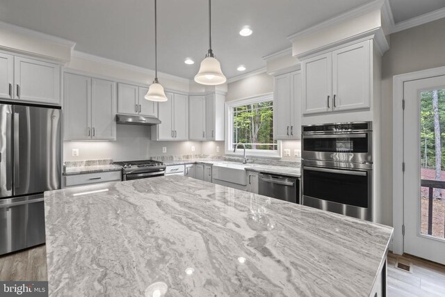 kitchen with light stone counters, crown molding, decorative light fixtures, a center island, and appliances with stainless steel finishes