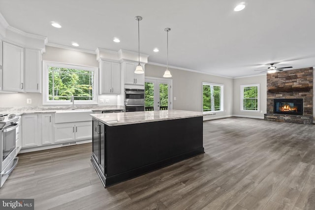 kitchen with appliances with stainless steel finishes, white cabinetry, sink, hanging light fixtures, and a center island