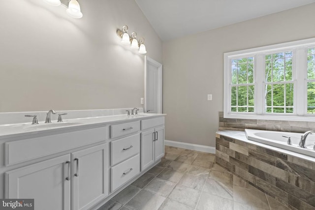 bathroom with vanity, a relaxing tiled tub, lofted ceiling, and a healthy amount of sunlight