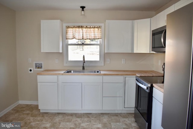 kitchen featuring stainless steel appliances, white cabinets, a sink, butcher block countertops, and baseboards