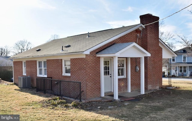 view of side of home with central AC, brick siding, a lawn, roof with shingles, and a chimney