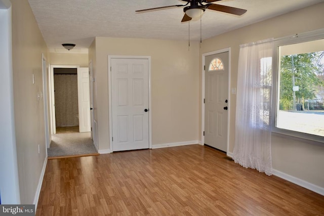 foyer entrance with a ceiling fan, baseboards, a textured ceiling, and light wood finished floors