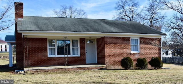 view of front of house with a shingled roof, a chimney, fence, a front lawn, and brick siding